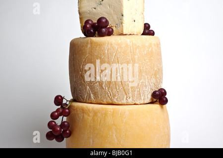 Two whole round cheeses with a large wedge of blue cheese in a tower with grapes Stock Photo