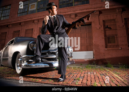 Gangster holding Tommy gun leaning on vintage car Stock Photo