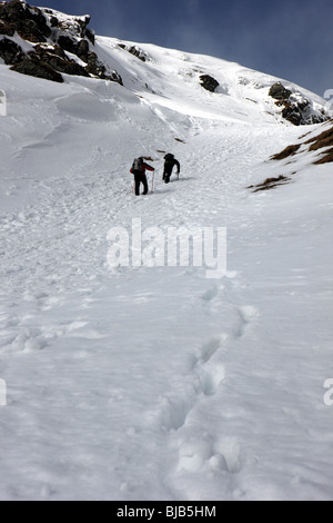 Two walkers climbing the snowy crags of Cam Chreag  towards the summit of Meall Nan Tarmachan Stock Photo