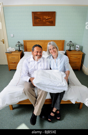 A couple running a bed and breakfast guesthouse sitting on a guests bed with fresh linen UK Stock Photo