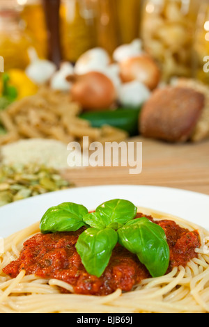Spaghetti Bolognese with basil garnish various Italian pasta and ingredients out of focus in the background. Stock Photo
