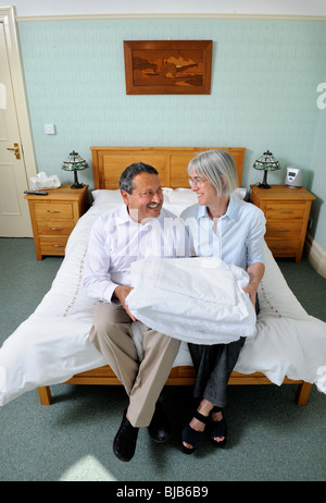 A couple running a bed and breakfast guesthouse sitting on a guests bed with fresh linen UK Stock Photo