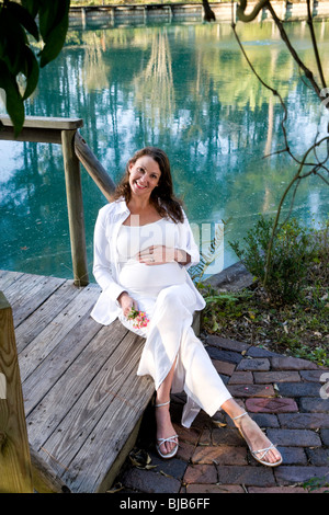 Pregnant woman sitting on wooden bridge in park Stock Photo