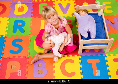 Little preschool girl playing with dolls on colorful alphabet mat Stock Photo