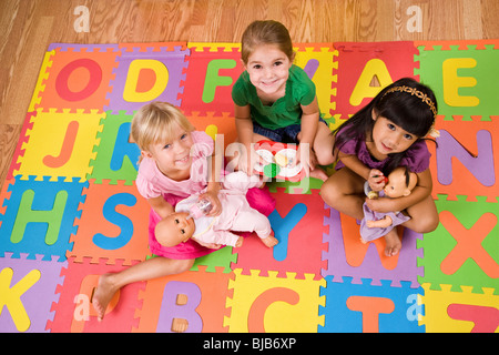 Little preschool girls playing with dolls on colorful alphabet mat Stock Photo