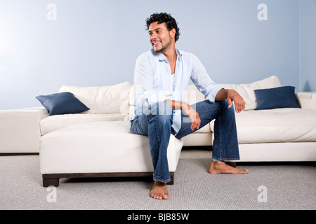 Young Hispanic man sitting at home alone on couch Stock Photo