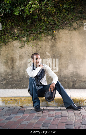 Handsome stylish young African-American man sitting on curb Stock Photo