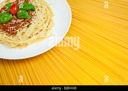 Plate of Spaghetti Bolognese with basil garnish, grated Parmesan cheese and plum tomato displayed on a fan of dried spaghetti Stock Photo