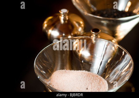 Salt and pepper displayed in open glasses, with metal pepper mills present. Stock Photo