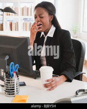 Mixed race businesswoman yawning at desk Stock Photo