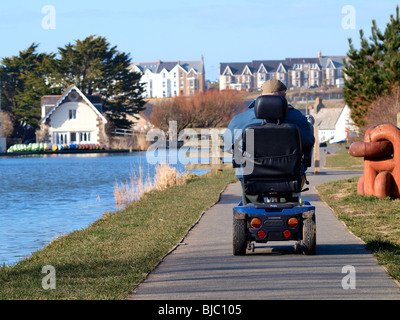 Old man on a mobility scooter riding along the canal path, Bude, Cornwall Stock Photo