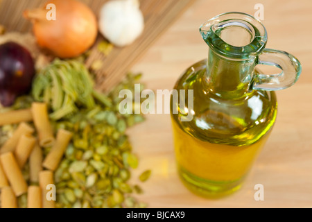 A bottle of extra virgin olive oil with dried pasta, red onions, white onions and garlic cloves out of focus in the background Stock Photo