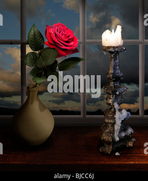 red rose on a window seal lighten by a candelabra Stock Photo