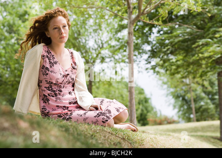 Young woman sitting on grass, looking away in thought Stock Photo