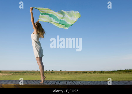Woman standing on deck, holding scarf up in breeze Stock Photo