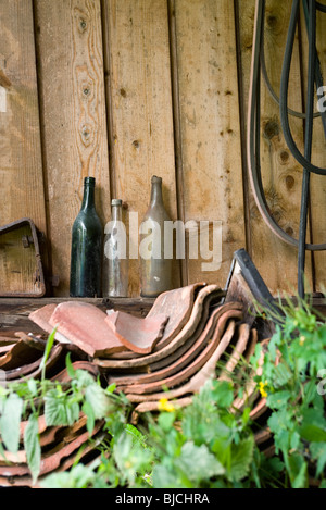 Old glass bottles, broken clay tiles stacked by wall outdoors Stock Photo