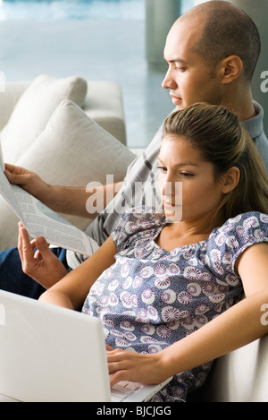 Couple relaxing together on sofa, man reading and woman using laptop computer Stock Photo