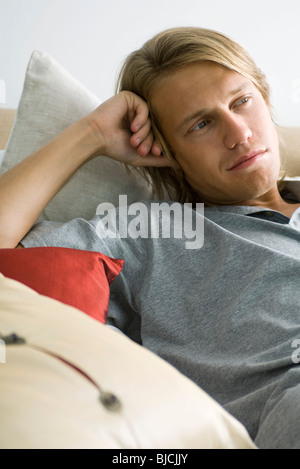 Man relaxing on pillows, looking away in thought Stock Photo