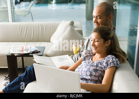 Couple sitting together on sofa, laughing at laptop computer Stock Photo