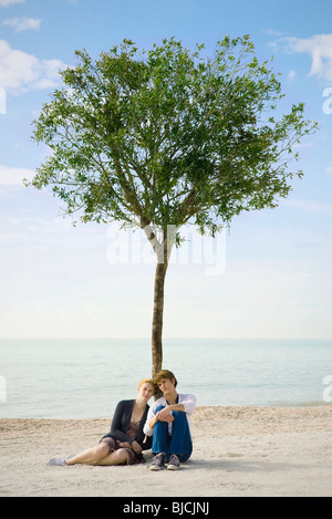 Young couple sitting together beneath tree on beach Stock Photo