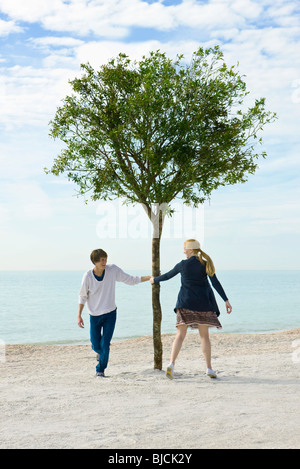 Young couple playfully pursuing one another around tree Stock Photo