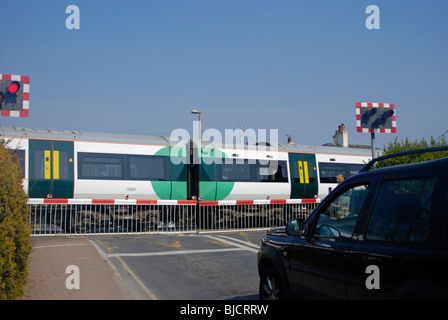 railway level crossing barriers down with a train speeding through Stock Photo