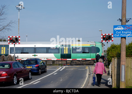 traffic building up with railway level crossing barriers down with a train speeding through Stock Photo