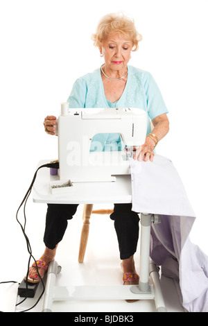 Senior woman using a sewing machine to sew curtains. Full body isolated on white. Stock Photo