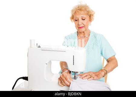Senior woman making curtains on a sewing machine. Isolated on white. Stock Photo
