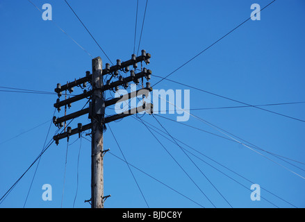 An old telegraph pole against a blue sky with telephone wires heading off in all directions. Stock Photo