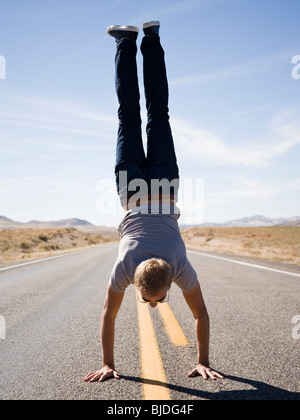 man doing a handstand in the middle of the road. Stock Photo