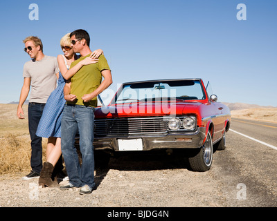 two men and a woman in front of a red convertible. Stock Photo