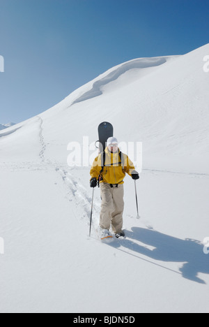 Snowboarder hiking with snow shoes carrying his board in off-piste terrain, Chamonix, France Stock Photo