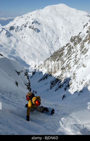 Snowboarder entering very steep gully at Col Belvede, near Le Brevent-Flegere ski resort, Chamonix, France. Mt Buet in distance. Stock Photo