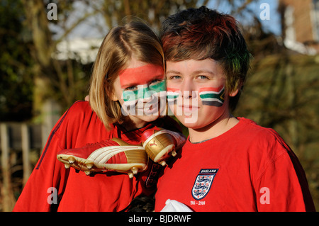 Young football supporters boy & girl wearing red England shirts with face painted faces in colours of the national flag of ZA Stock Photo