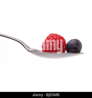 Raspberry and Blueberry sitting in bowl of stainless steel spoon isolated against white background. Stock Photo