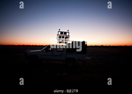 IR lighting rig wagon silhouetted by the setting sun prior to a night film shoot in Africa Stock Photo