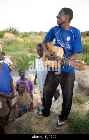 A young man plays a guitar in a field in Amuria, Uganda, East Afica. Stock Photo