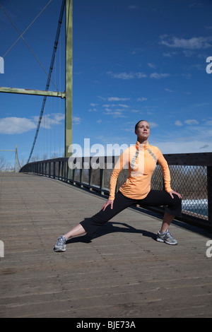 Woman runner stretching on a pedestrian bridge in a city park Stock Photo