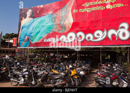 India, Kerala, Kollam Junction Railway Station, motorcycles parked under huge advertising hoarding Stock Photo