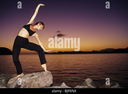 Woman practising yoga on rocks at the beach Stock Photo