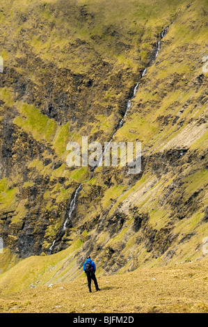 A walker contemplates a long thin waterfall in the Sheeffry Mountains, County Mayo, Ireland Stock Photo