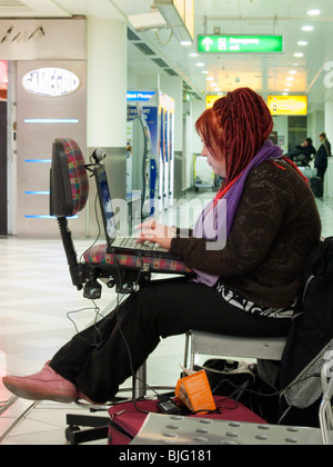 A female airline passenger using a laptop computer in an airport transit area with waiting passengers in the background. Stock Photo