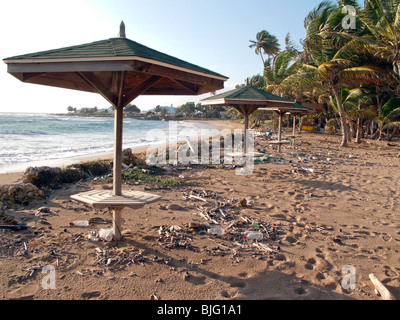 A setting sun on a rubbish strewn Caribbean beach with deserted shady tables empty plastic bottles and wind blown debris Stock Photo