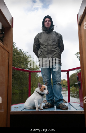 A narrow boater and his dog traveling in showery weather on the Rochdale canal, Yorkshire. Stock Photo