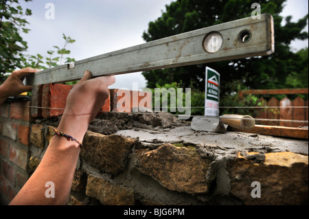 Using a spirit level during the building of a garden wall with cotswold stone and cement mortar UK Stock Photo