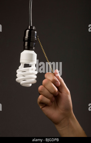 hand pulling chain on energy saving light bulb Stock Photo