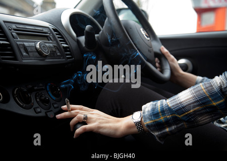 Woman smoking cigarette in car. Doctors in UK are calling for a ban of smoking in cars. Stock Photo