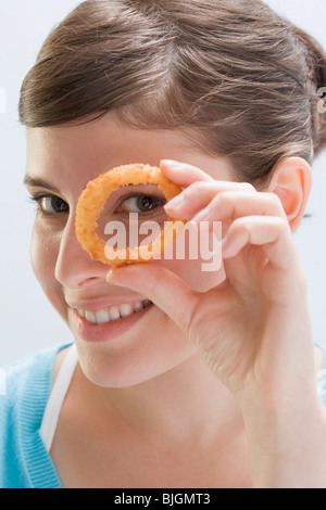 Young woman looking through deep-fried onion ring - Stock Photo