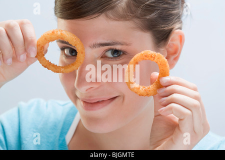 Young woman holding up two deep-fried onion rings - Stock Photo